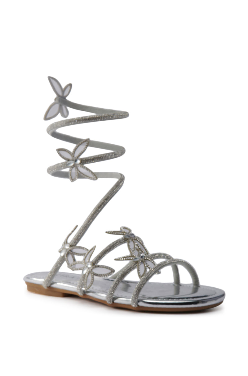 The AKIRA ALBUS SILVER COIL RHINESTONE FLAT SANDAL is a shining faux leather flat with rhinestones, floral accents, butterfly appliques, and an elegant spiral ankle strap wrapping up the leg. 4