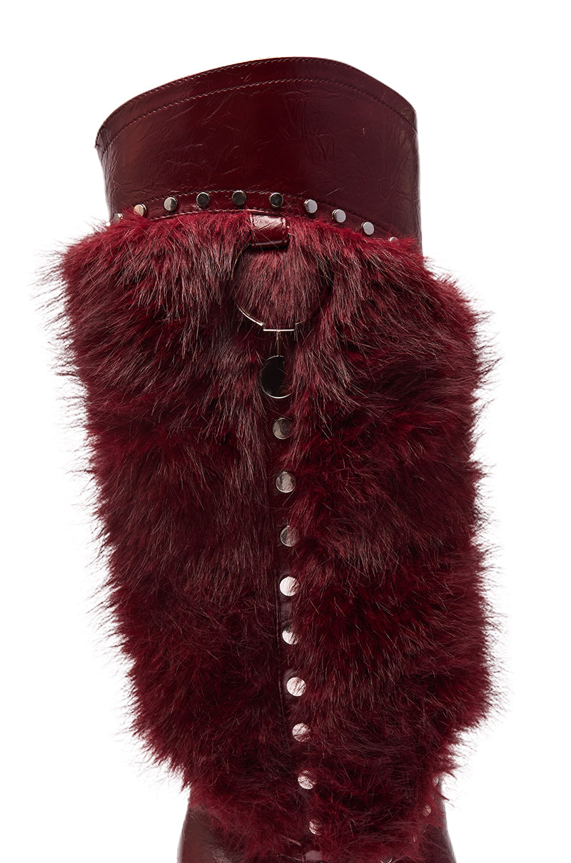 The AZALEA WANG ALISETTE BURGUNDY MIXED MATERIAL FUR AND SNAKE STILETTO BOOT is a knee-high, burgundy boot with plush dark red faux fur, silver studs at the top, and metallic accents down the center.