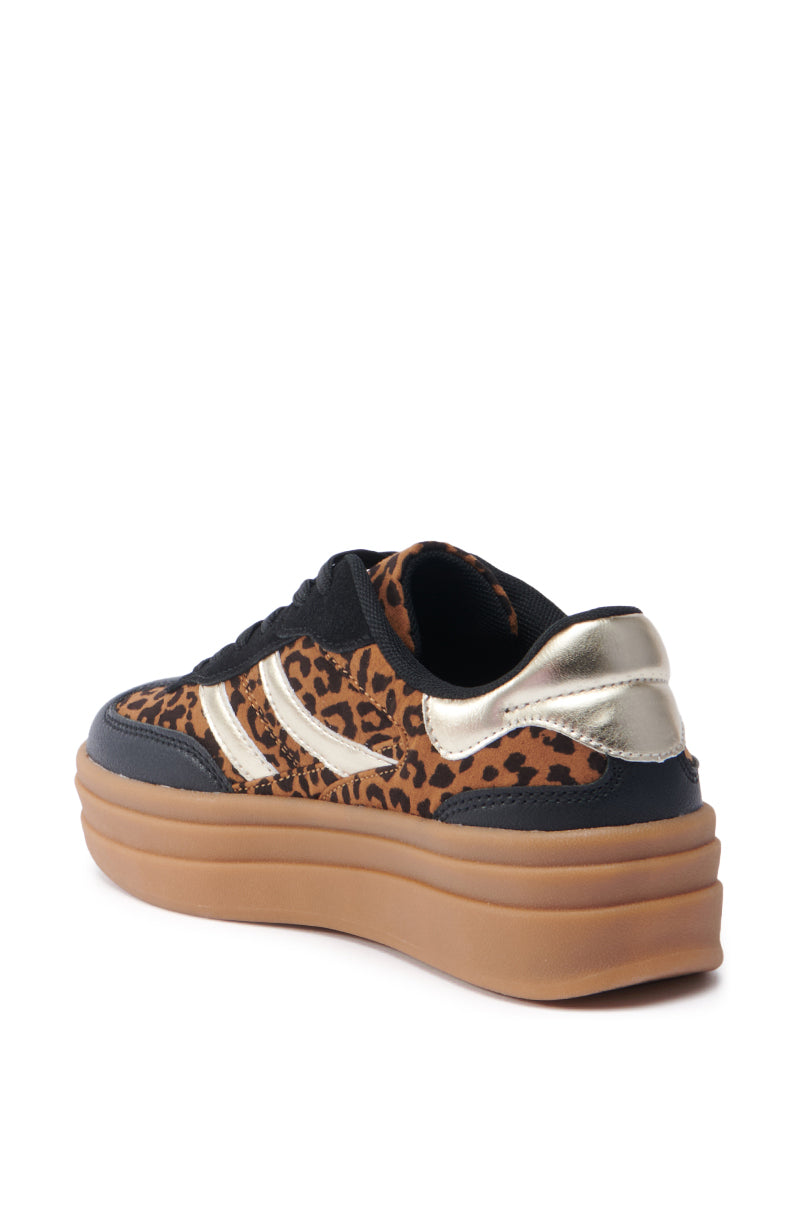 The AZALEA WANG ALPACA MULTI LEOPARD PLATFORM SNEAKER boasts metallic leather accents on the heel and stripes, complemented by a black faux suede base and a thick brown sole. The sneaker is presented from an angled back view, blending bold style with modern flair. 5