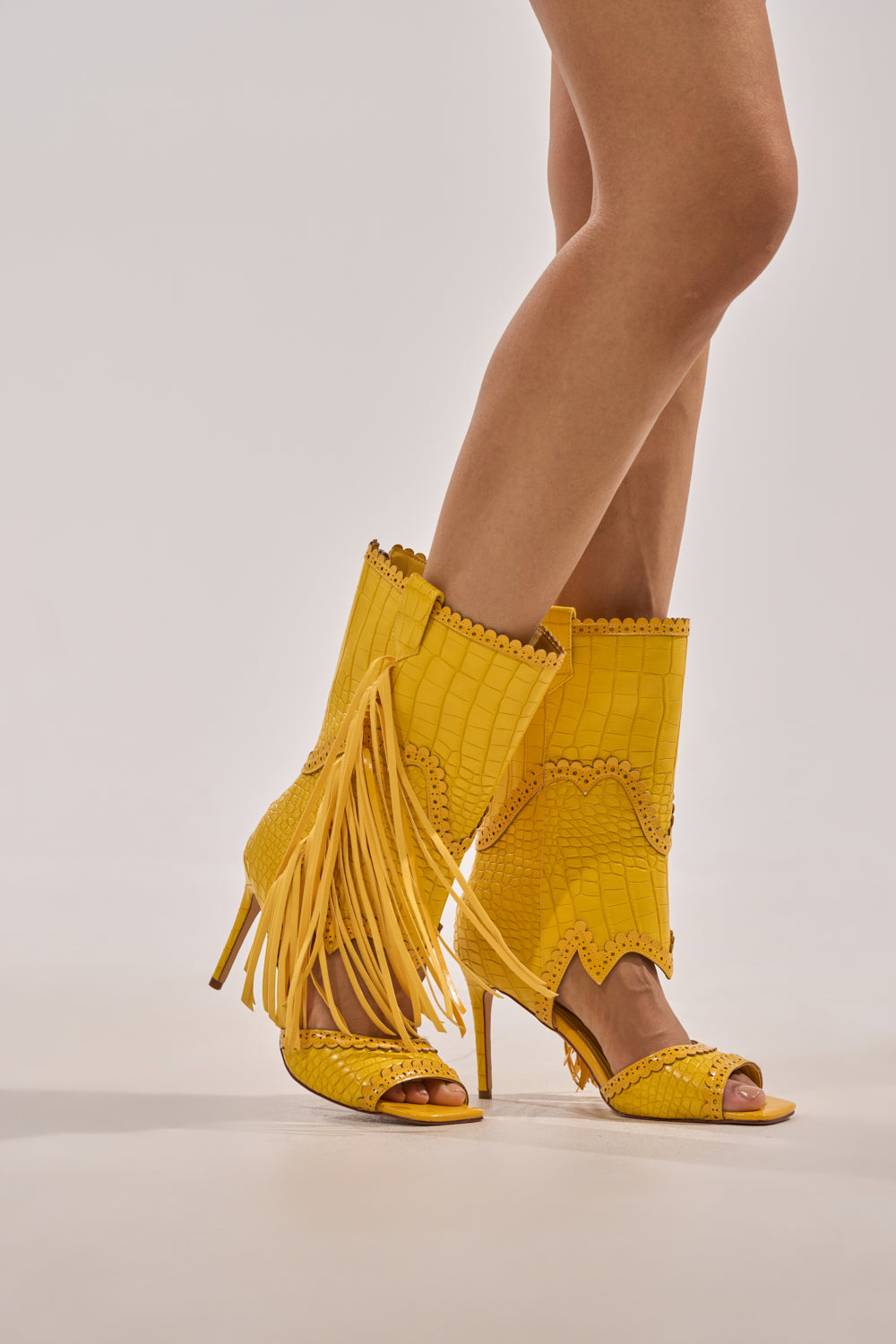 A person wearing the AZALEA WANG ALPHONSE YELLOW OPEN TOE SANDAL stands on a light-colored floor with their legs crossed at the ankles. 8
