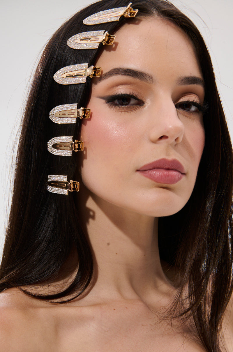 A woman with long dark hair and flawless makeup wears TOO PRETTY FOR THIS BLING HAIR CLIPS—five sparkling rhinestone clips arranged in a curved line on one side. The background is plain and light.