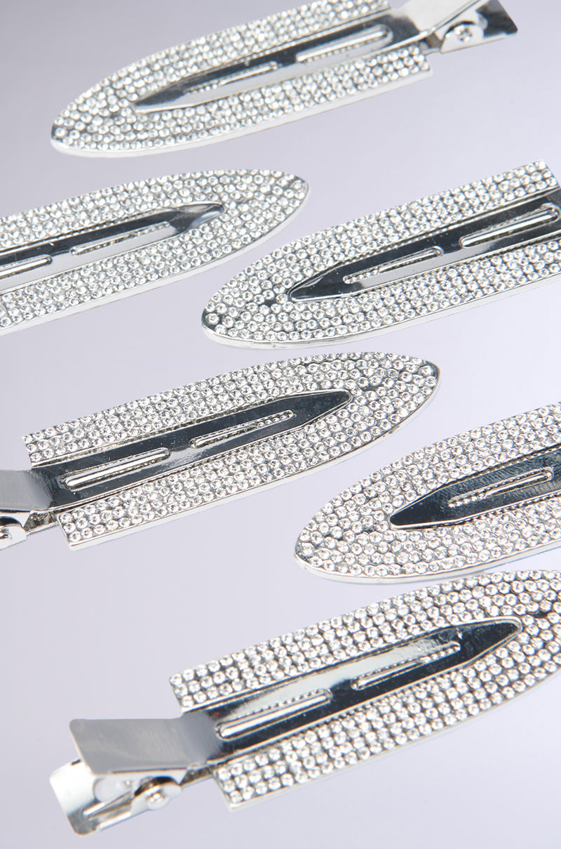 Close-up of several TOO PRETTY FOR THIS BLING HAIR CLIPS, adorned with small, sparkling rhinestone embellishments, arranged in a scattered pattern on a smooth, light gray surface. 6