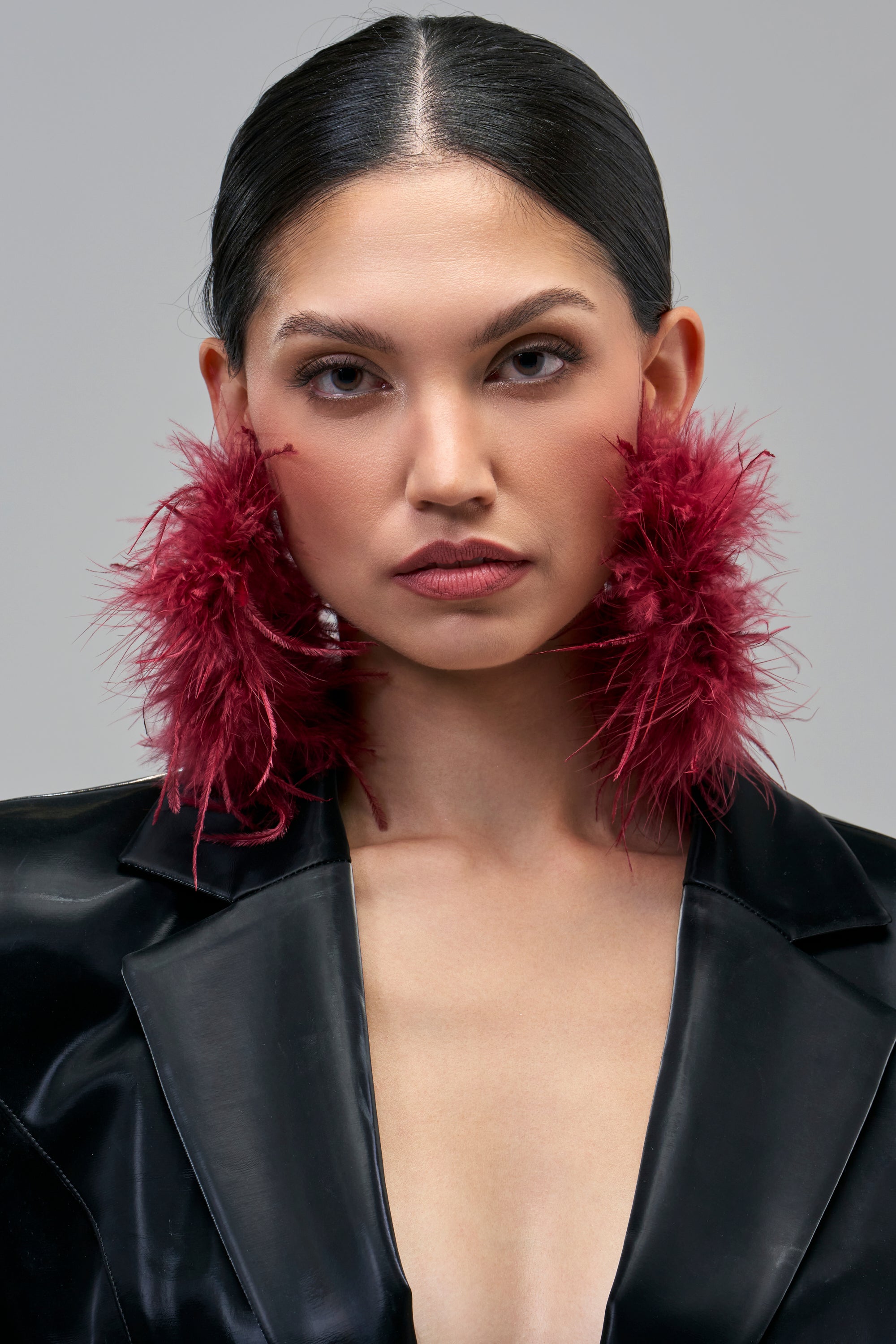A person wearing large, deep burgundy OXBLOOD FEATHER HOOP earrings as a statement accessory.