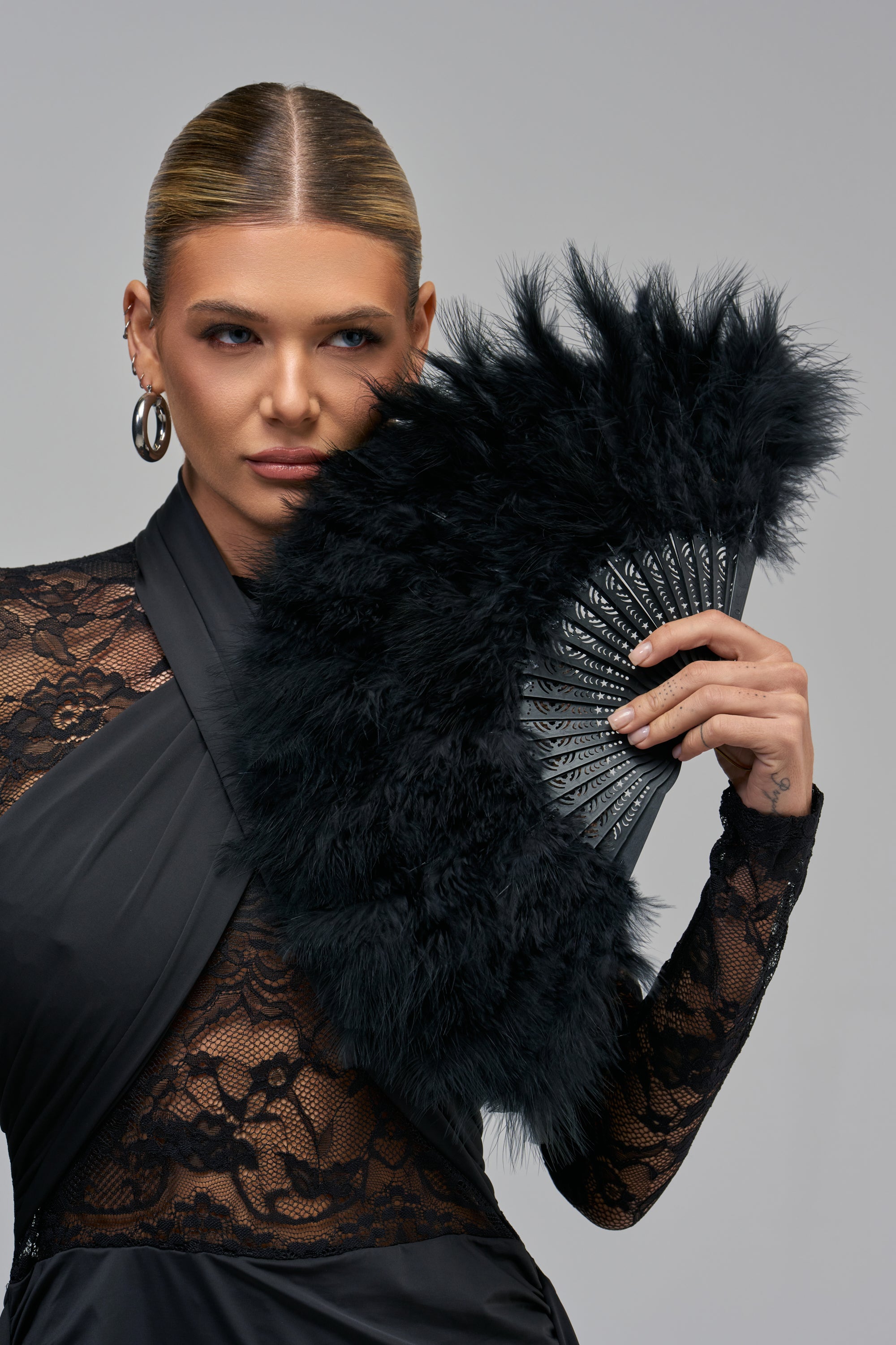 A woman holding a black FIND LESS FEATHER FAN in front of her face.