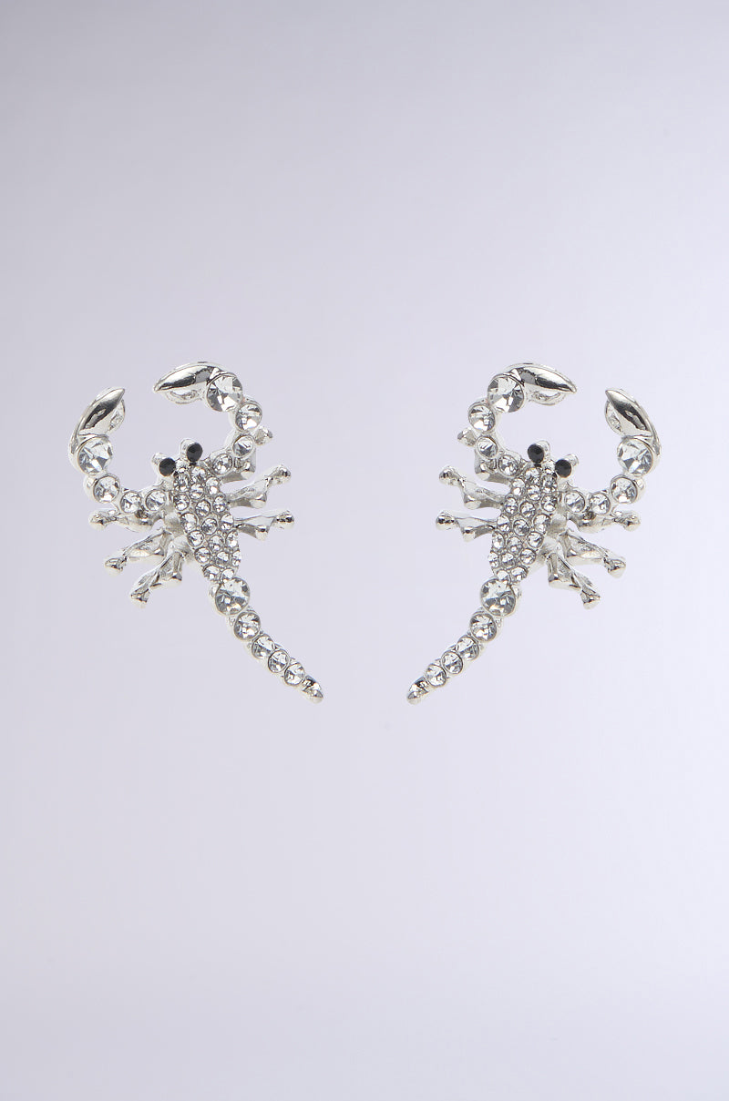 The CLAWS UP EARRING features silver scorpion shapes with intricate details and rhinestone accents, set against a light gray background. 0