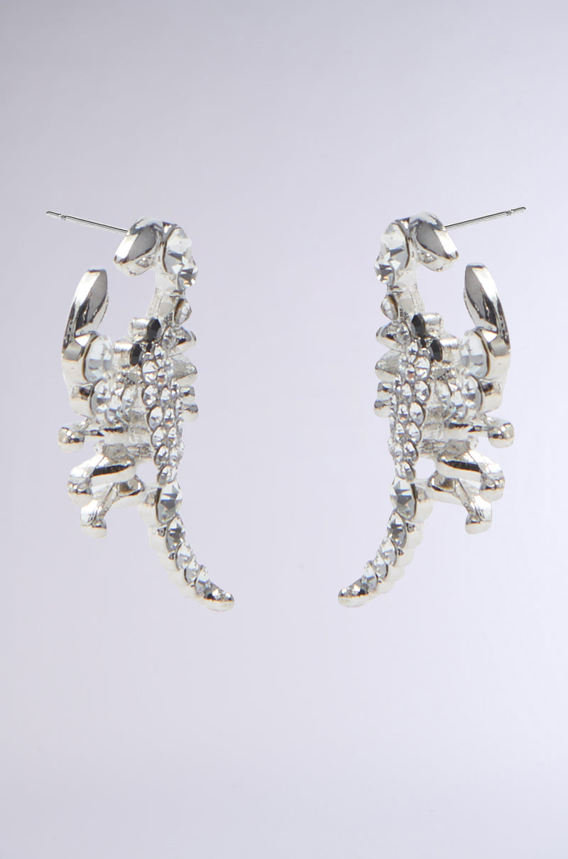 The CLAWS UP EARRING features rhinestone-adorned, scorpion-shaped designs in shiny faux silver, set against a plain light gray background. 2