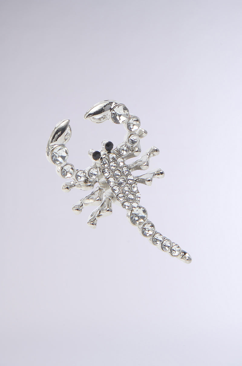 The CLAWS UP EARRING showcases an intricately designed faux silver scorpion, featuring detailed claws, legs, and a rhinestone-adorned segmented tail. Set against a gray background, its small black eyes provide a striking contrast. 3