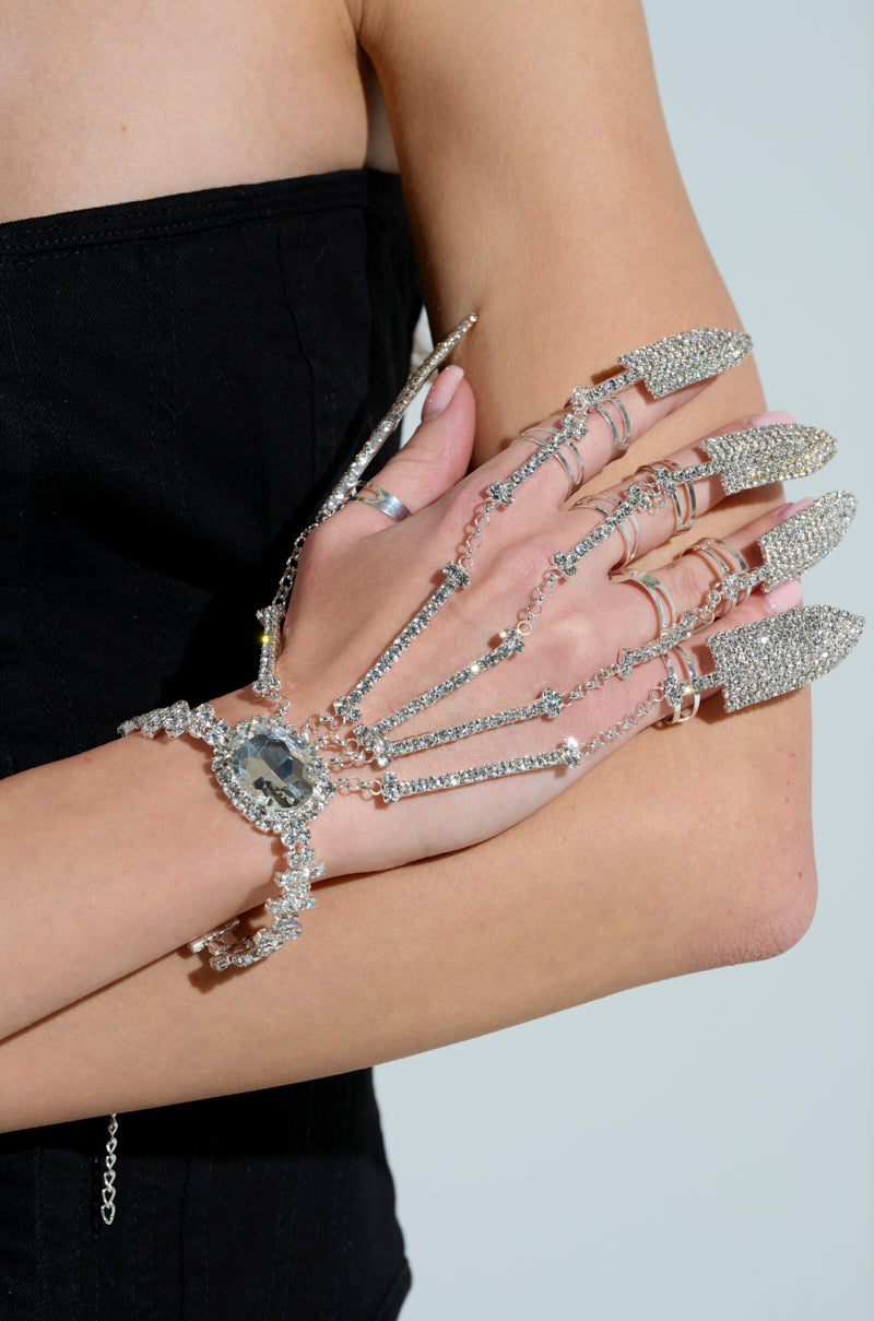 A person in a black top flaunts the CLAW MY WAY BLING RING SET, featuring skeleton finger-like rhinestone encrusted attachments crafted from faux silver chains, elegantly covering their hand and fingers. 2