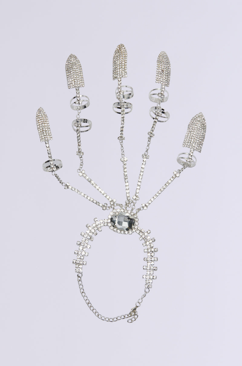 The CLAW MY WAY BLING RING SET is a silver hand accessory with five finger extensions, intricate chains, and ornate rings forming a skeletal design. Rhinestone accents add sparkle, and its centerpiece on the palm features a large rectangular gemstone against a plain white background. 3