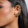 Their right ear features the I BOUNCE BACK EAR CUFF, a striking faux gold accessory with stylized spikes. Straight brown hair complements a black textured garment.