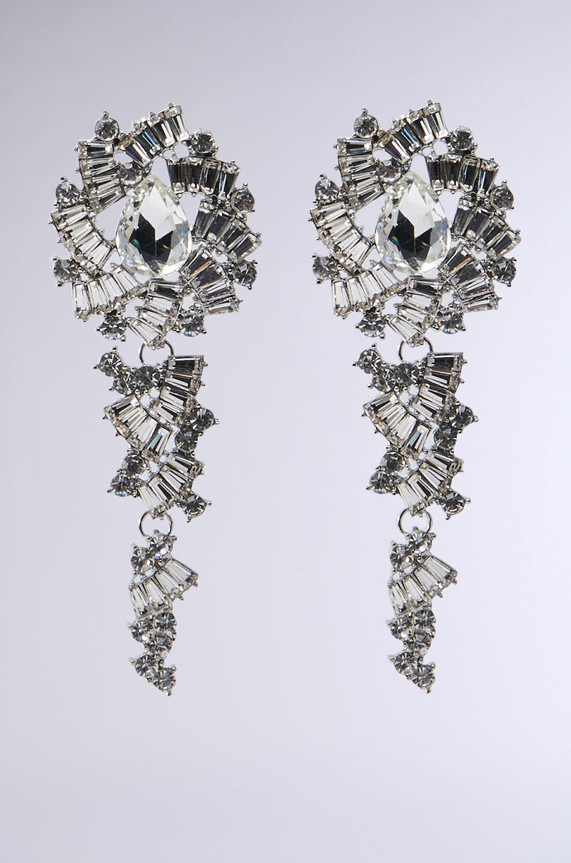 The BEATRICE EARRING exudes opulent elegance with its intricate design of sparkling gemstones. A large central gem is surrounded by smaller rhinestones, arranged in an ornate pattern against a neutral background.