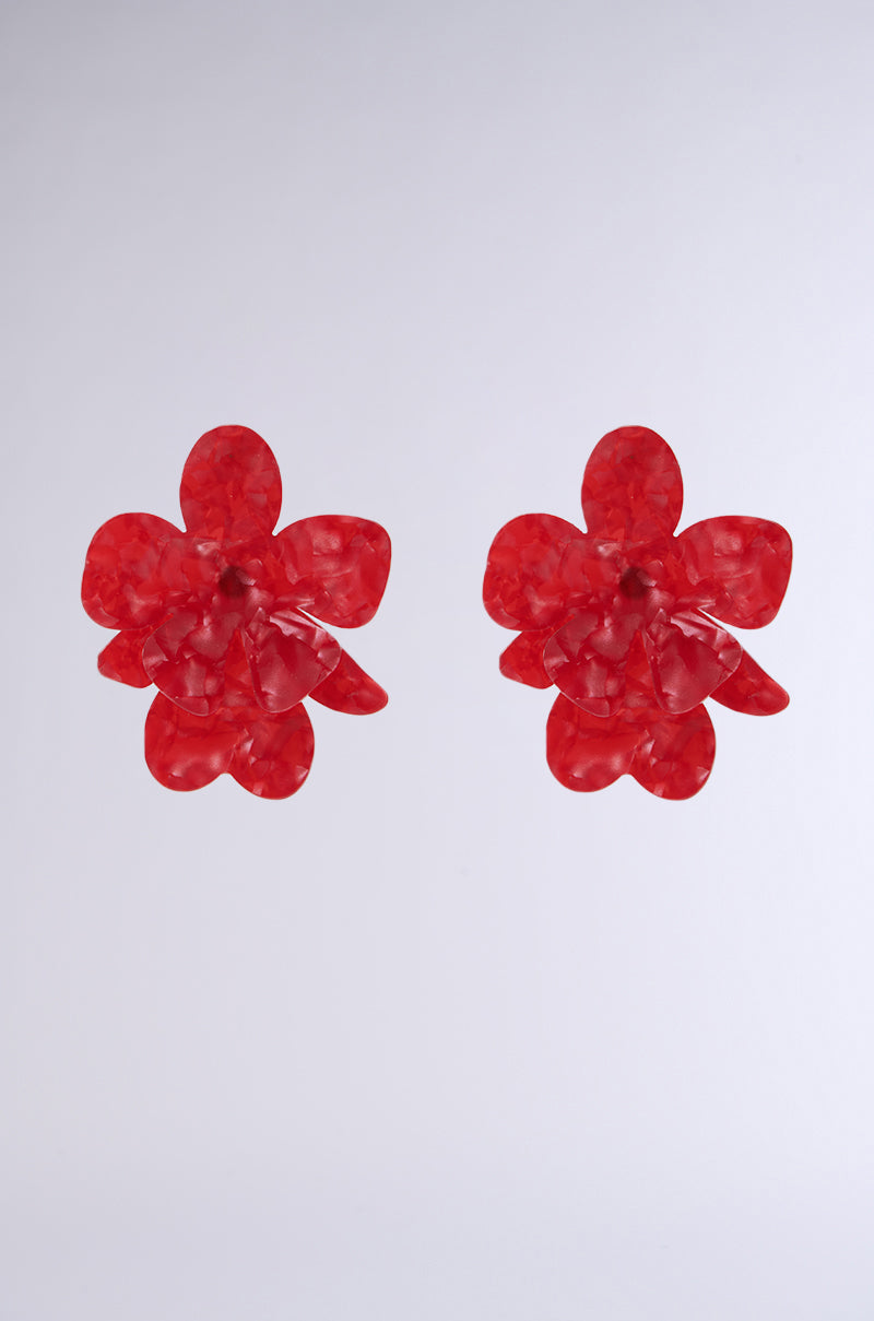 The ROSY EARRING IN RED features marbled red resin crafted into flower shapes with five petals and a textured surface on a plain gray background. These earrings add elegance and charm, making them perfect for your Valentine's Day ensemble.