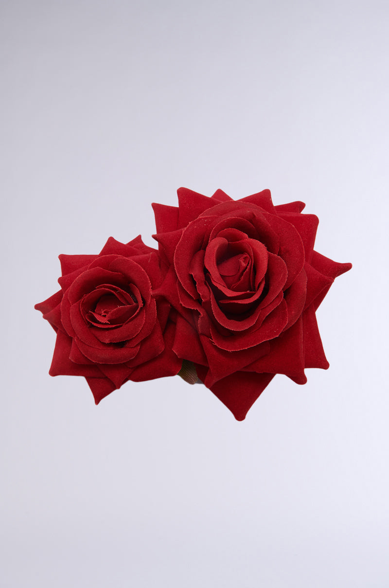 Two red roses with velvety petals, one slightly larger than the other, are set against a plain light gray background. Similar to the DOLCE VITA ROSE HAIR CLIP, these blooms display their layered petals and deep red color, making them ideal for a chic hair accessory statement. 2