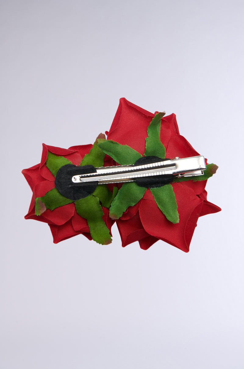 The DOLCE VITA ROSE HAIR CLIP is a captivating hair accessory adorned with two red fabric roses and green leaves. This sophisticated metallic barrette is showcased horizontally against a simple white background, exuding timeless elegance. 3