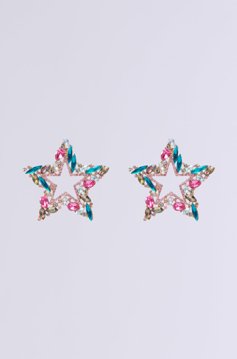 The "I AM THE MOMENT EARRING" is a pair of star-shaped earrings featuring multi-color gemstones and radiant rhinestone insets with pink, blue, and gold hues, all set against a simple light background.