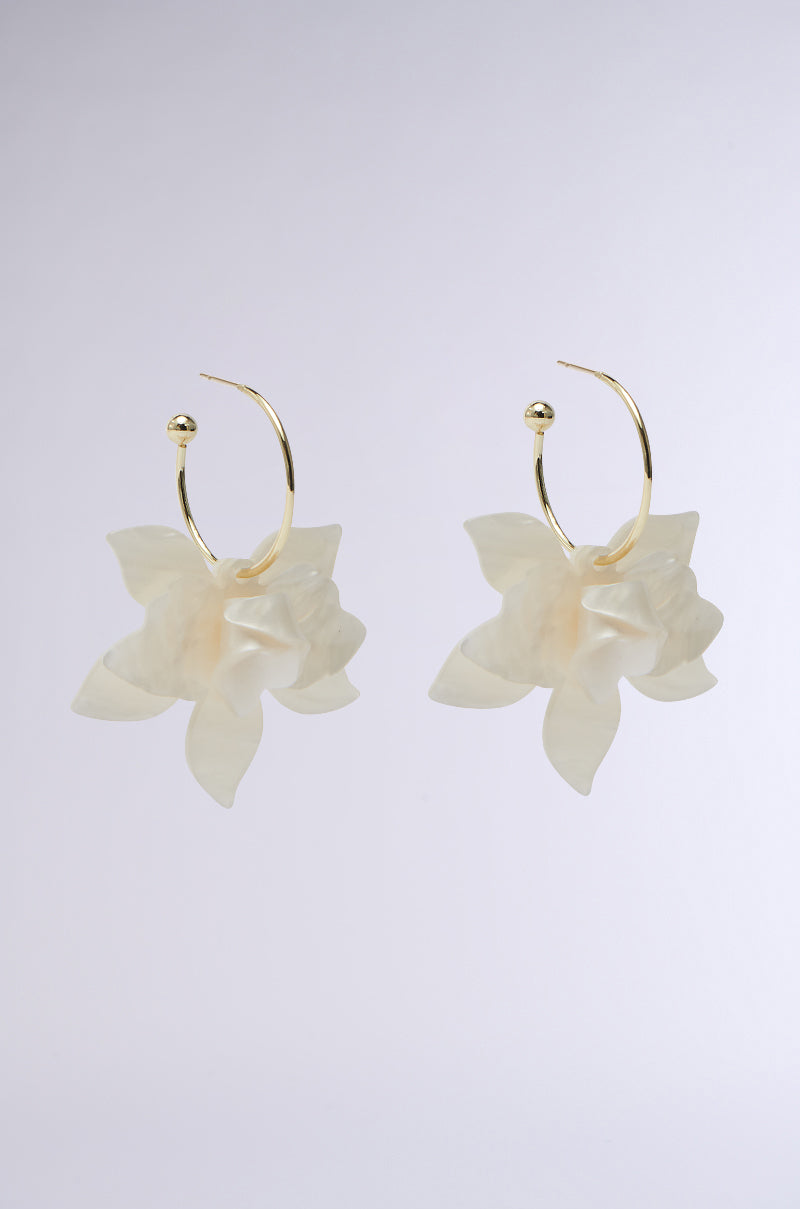The WHITE FLORAL HOOP EARRING showcases gold hoops with pearlescent flower petals forming large pendants. Displayed on a light gray backdrop, these botanical beauties highlight an elegant design.