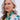 A woman with long gray hair and blue eyes wears a floral dress and WHITE FLORAL HOOP EARRING with pearlescent petals. She stands against a light background, her neutral expression embodying true botanical beauty style.