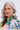 A woman with long gray hair and blue eyes wears a floral dress and WHITE FLORAL HOOP EARRING with pearlescent petals. She stands against a light background, her neutral expression embodying true botanical beauty style.