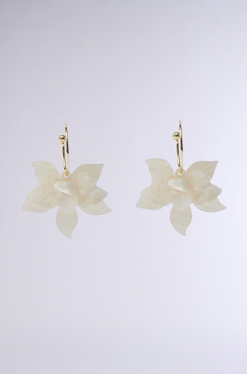 The WHITE FLORAL HOOP EARRING elegantly features beige, pearlescent flower petals hanging from small gold hoops, set against a plain gray backdrop.
