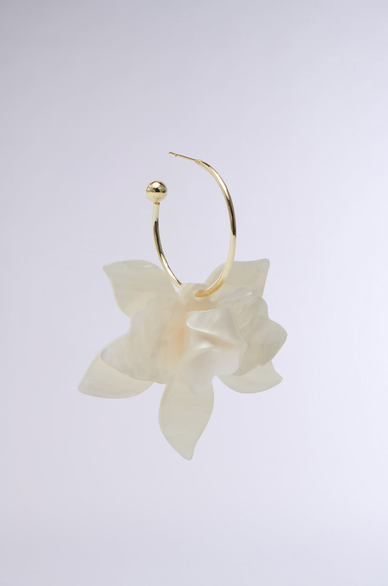 The White Floral Hoop Earring features a gold hoop with a translucent, pearlescent flower, exuding elegance with its botanical beauties and light gray backdrop.