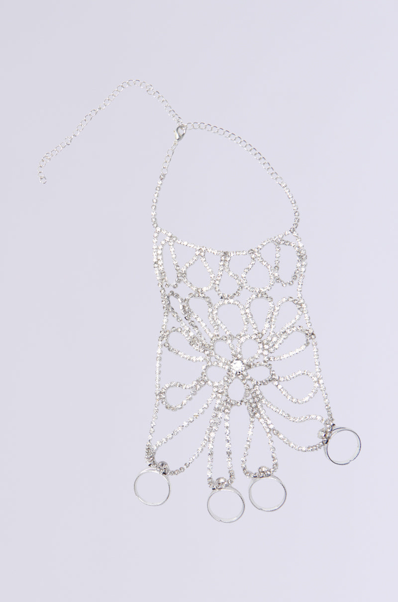 The I DESERVE IT ALL BRACELET AND RINGS set is a silver chain body harness with floral patterns and features three circular rings at the bottom. Rhinestone links add sparkle as it is displayed flat on a light gray background. 1