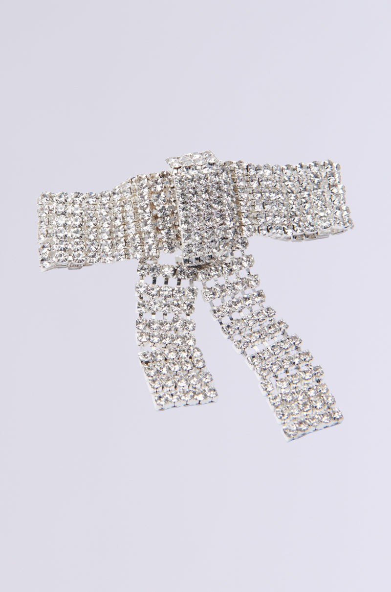 The TIE WITH A BOW STATEMENT RING features a sparkling, silver rhinestone bow-shaped design with a textured surface on a white background, showcasing intricately arranged stones that shimmer in the light for an effortlessly elegant ensemble.