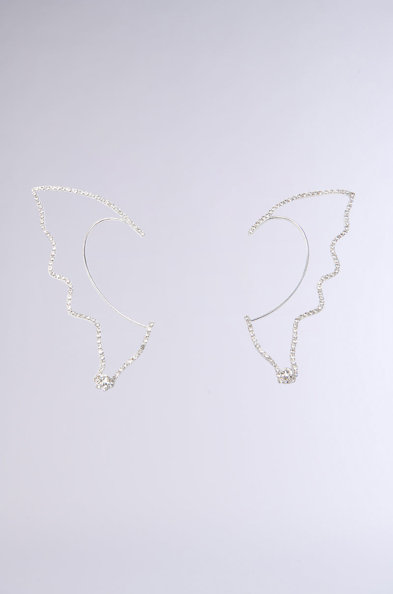 The TAKE FLIGHT EAR CUFF SET features two delicate, silver, wing-shaped ear cuffs with a minimalist asymmetrical design, displayed against a plain light gray background.