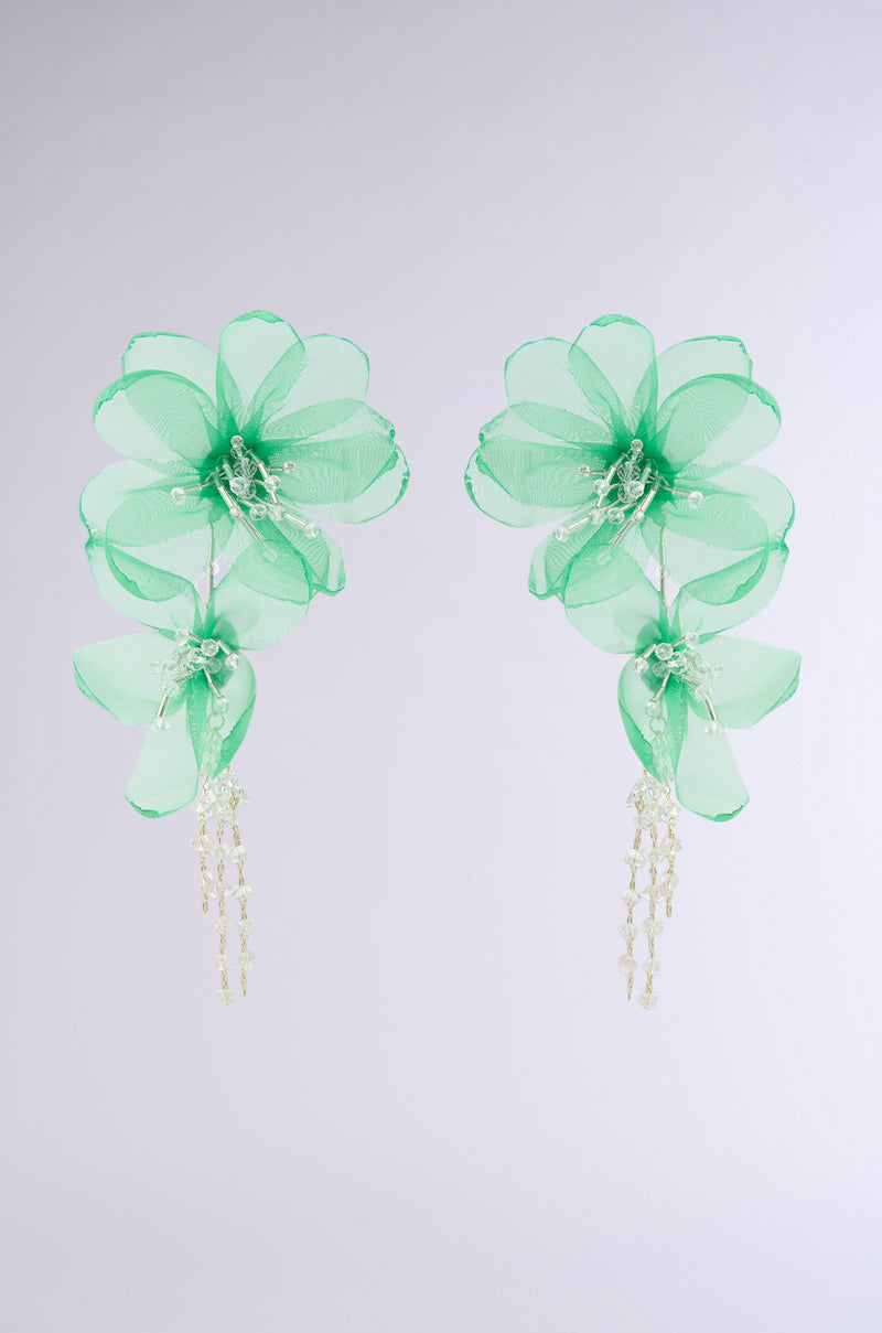 Check out the FLOWER POWER EARRING featuring dangle green floral earrings with beaded centers and sheer fabric petals, adorned with delicate cascading strands, making a striking impression on a plain white background.