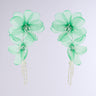 Check out the FLOWER POWER EARRING featuring dangle green floral earrings with beaded centers and sheer fabric petals, adorned with delicate cascading strands, making a striking impression on a plain white background.