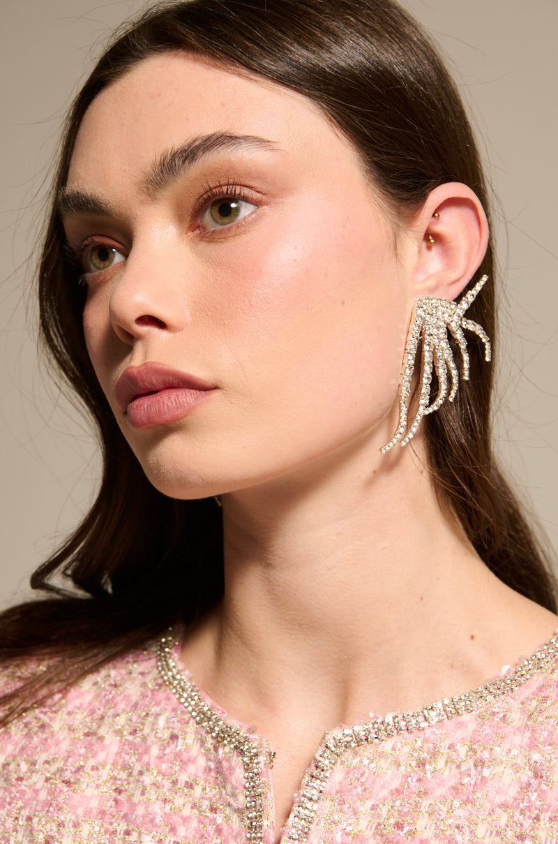 A woman with long brown hair wears the IN MY ZONE SILVER EARRING featuring sparkling rhinestone strands and a pink tweed top with jeweled trim. With light makeup, she looks calm as she gazes slightly to the side. 5