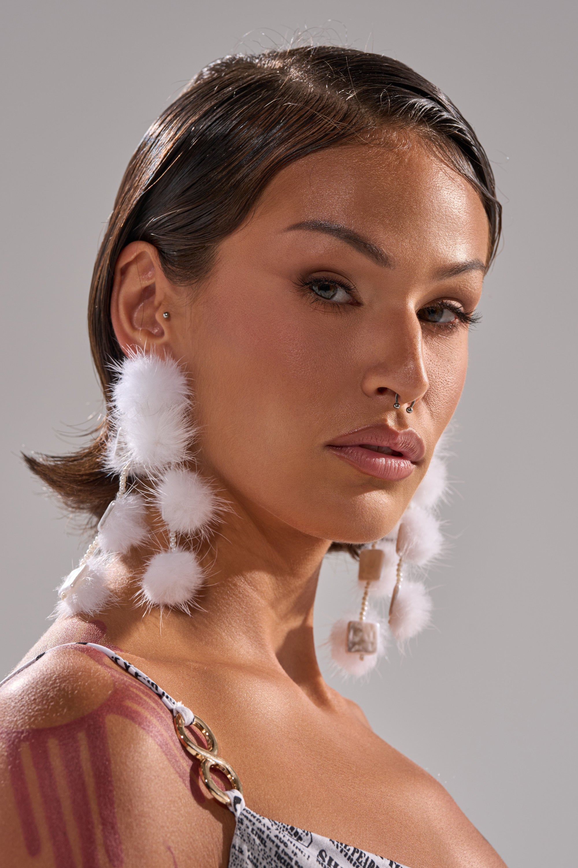 A person with short, sleek brown hair wears the bold SNOW PRINCESS EARRING, a septum ring, and a graphic spaghetti strap top. Their natural makeup and confident look make these chic winter accessories stand out. 0