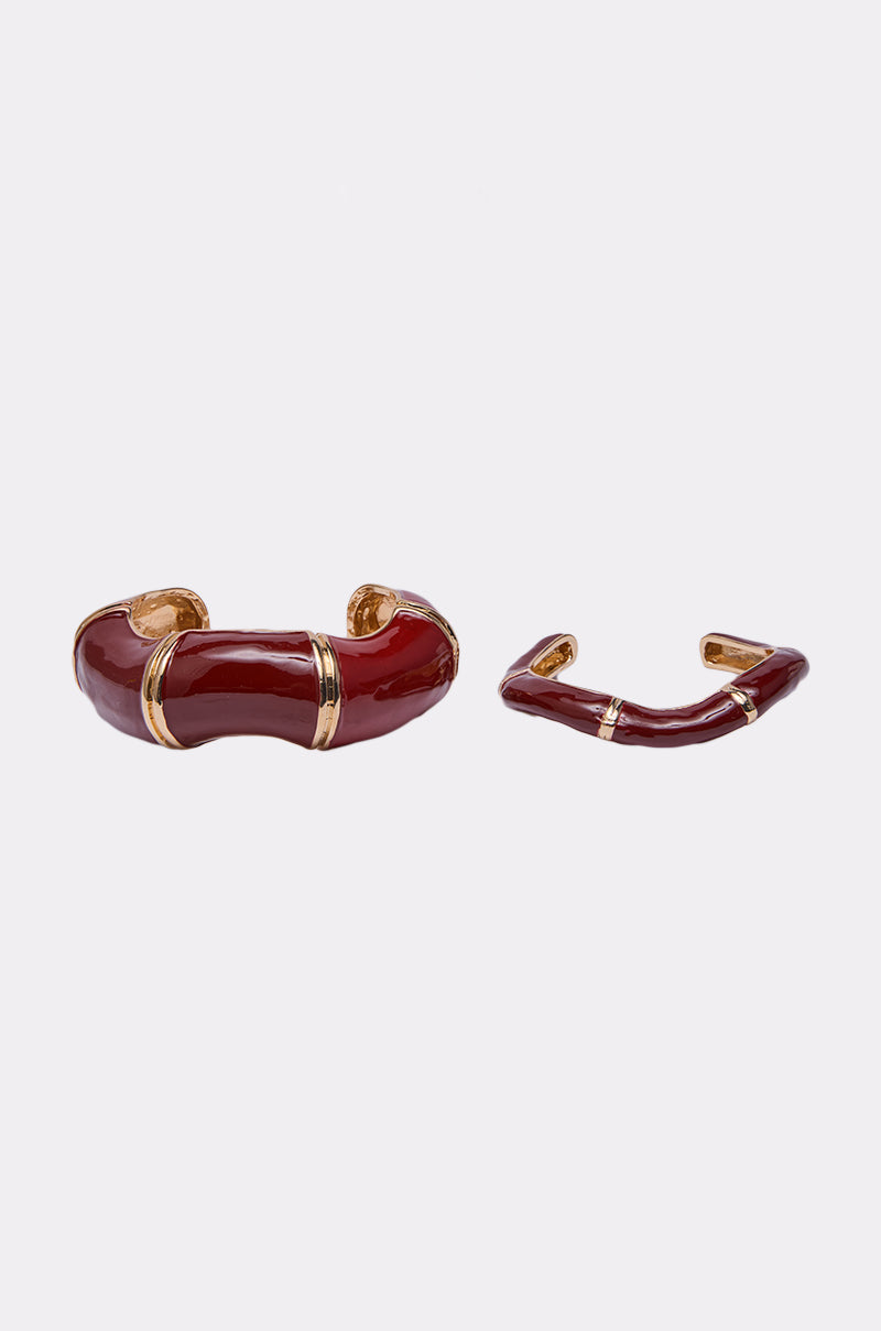 The LOLA BRACELET SET features two shiny red enamel bracelets with gold-tone accents: one chunky, curved bangle and a smaller, more angular piece, both displayed on a light background. 2