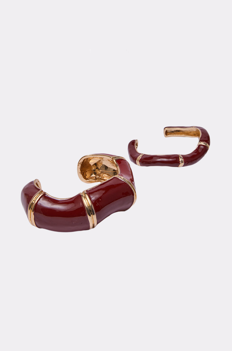 The LOLA BRACELET SET includes two chunky bangles in gold and deep red enamel, featuring a bamboo-inspired design with curved segments and gold accents, displayed on a white background. 3