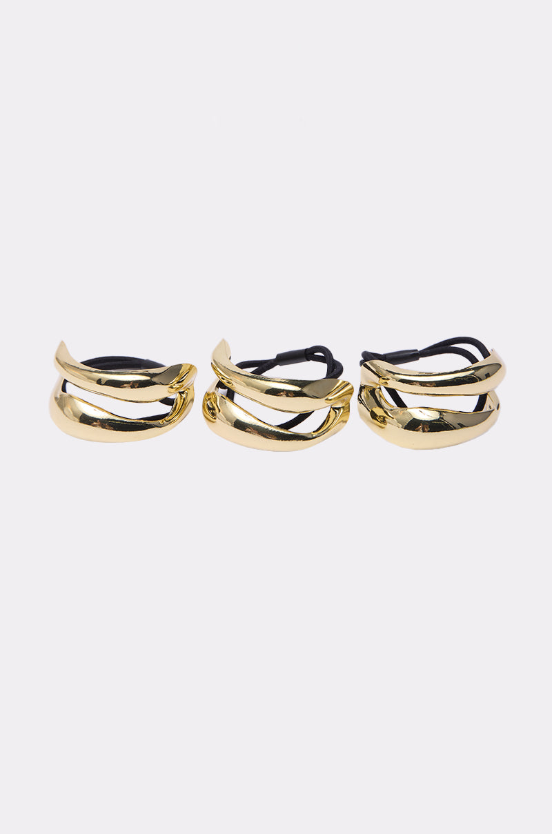 The GOLDEN RULE HAIR TIE SET features three gold-tone cuffs with twisted, overlapping metal designs, ideal for creating a chic bubble-pony style. Shown side by side on a plain white background.