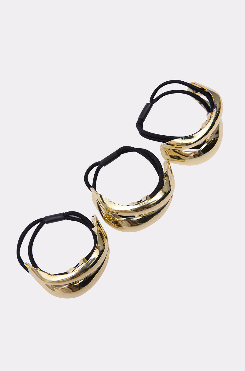 Three shiny gold metallic masks with black elastic straps are arranged diagonally on a white background, reflecting the sleek style of the GOLDEN RULE HAIR TIE SET.