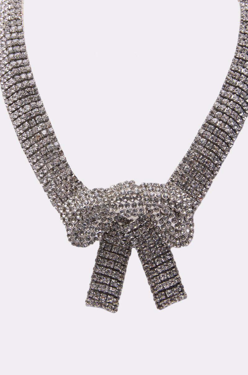 The GABBY BOW NECKLACE features a silver bow with a rhinestone centerpiece and sparkling stones in a grid pattern on the strap and bow—an elegant statement piece for any occasion. 2