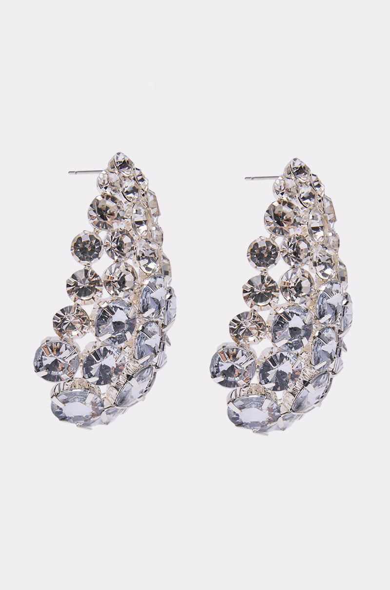 The NIGHT IS YOUNG EARRING is a pair of silver, curved evening earrings adorned with multiple rows of sparkling round clear rhinestones arranged in a graduated pattern. 2