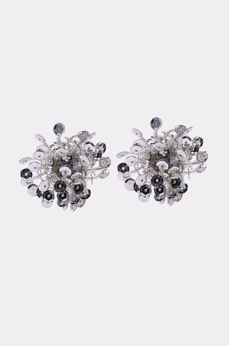 The STELLAR EARRING features silver-tone bead earrings with clustered leaf-like shapes and small round black accents in a floral, 3D design on a light background. 1