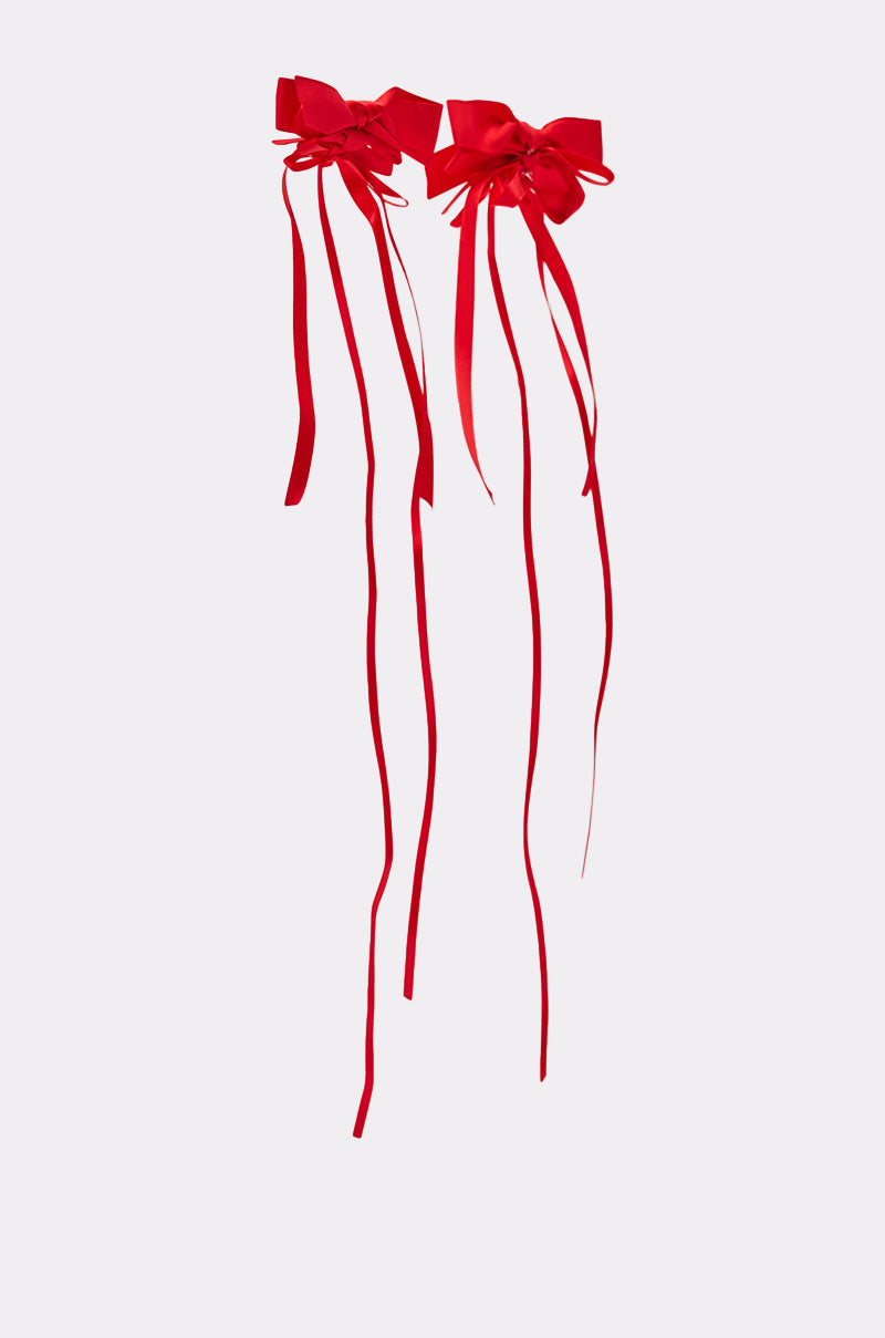 Two LACED UP EARRINGs, each featuring red satin ribbons with long trailing tails, are displayed side by side against a plain light gray background, their elegantly laced-up ribbons hanging down. 3