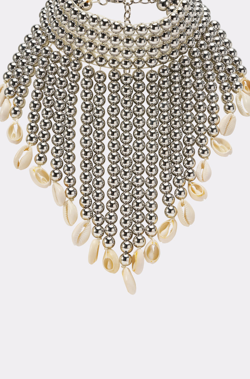 The TOO CHIC SEASHELL NECKLACE features metallic beads and multiple strands with small white cowrie shells at the ends, shown against a white background. 4