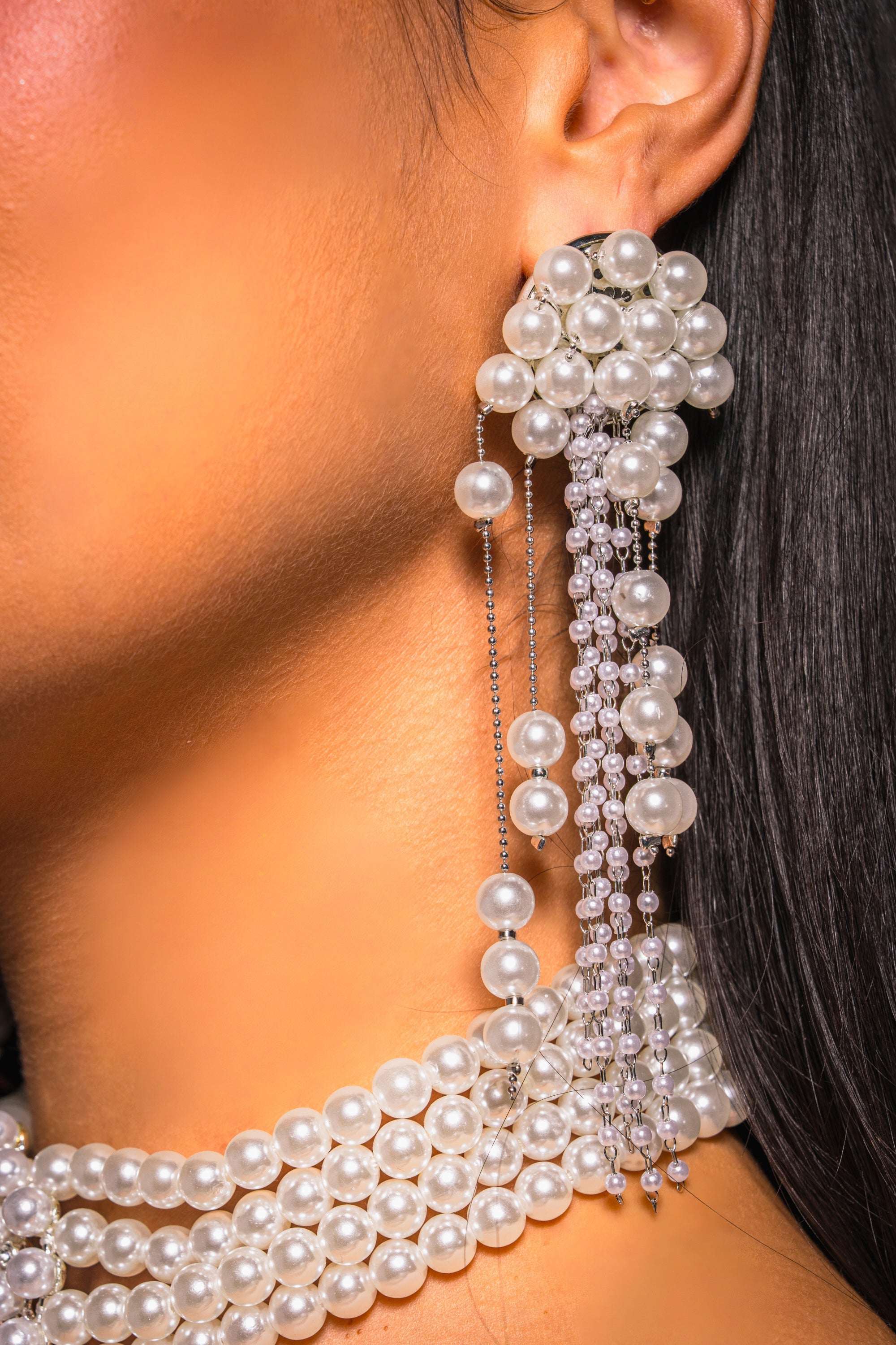 Close-up of a woman's ear and neck wearing the DRIPPIN IN PEARLS EARRING, featuring elegant pearl tassels with cascading strands, paired with a multi-strand pearl necklace—ideal statement jewelry for special occasions. 1