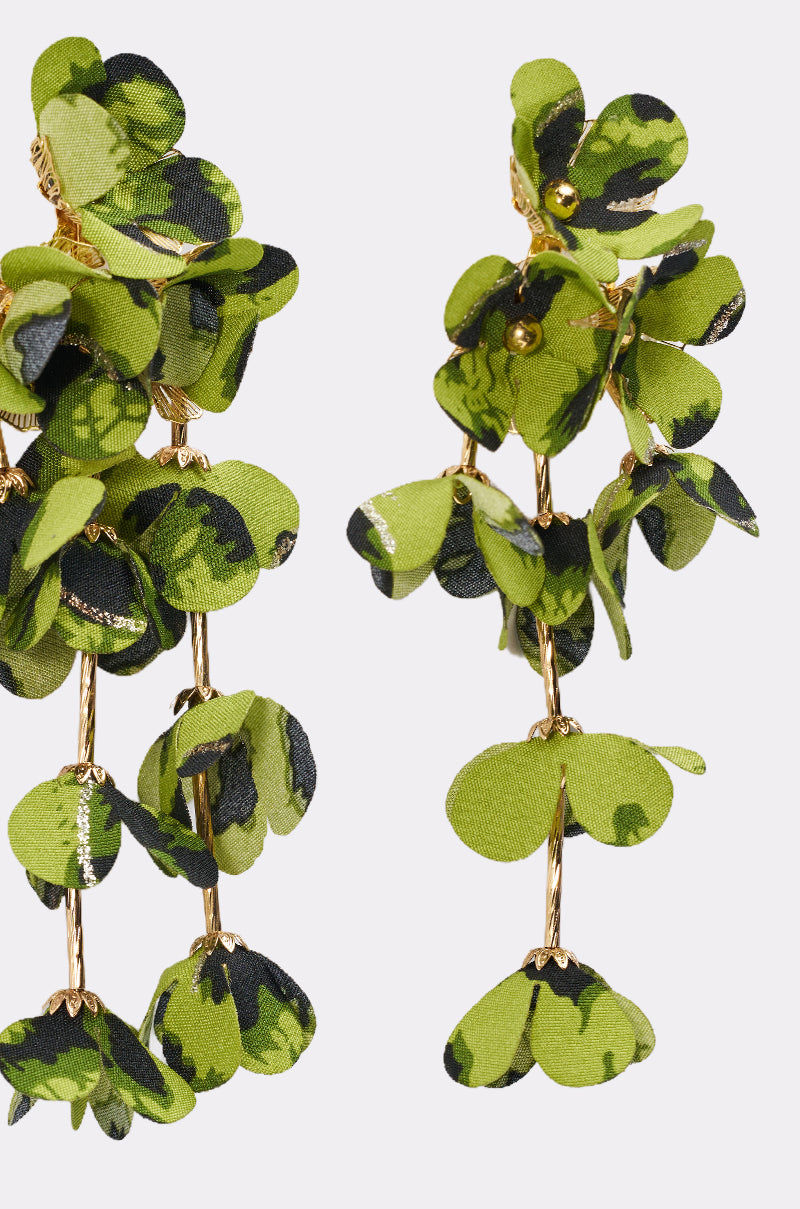 A close-up of the CATCH ME IF U CAN EARRING, statement earrings with clusters of green fabric leaves with dark spots on gold-colored wires, resembling cascading foliage. 4