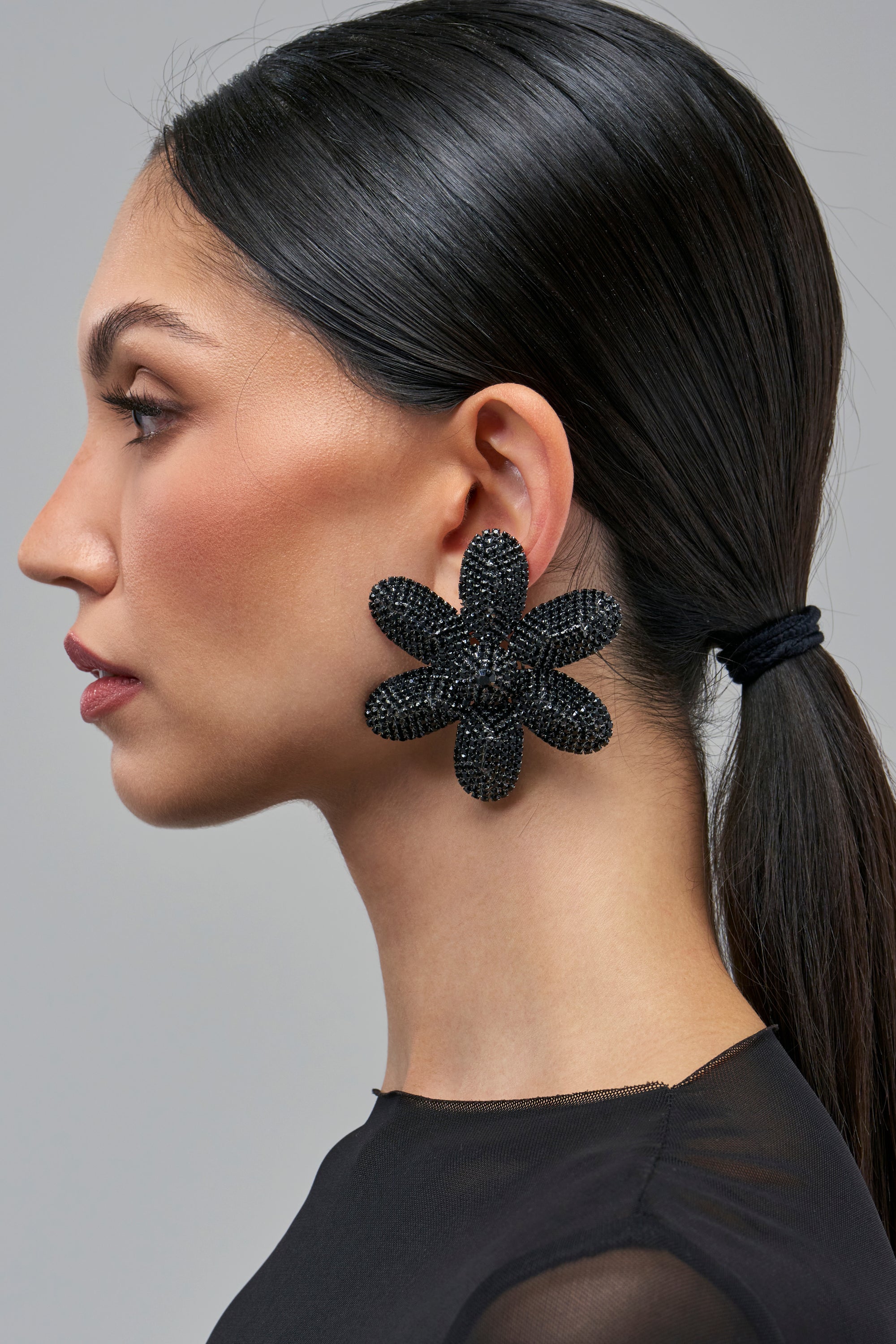 Profile view of a person wearing DARK ROMANCE EARRINGS, which are oversized, six-petaled black floral earrings covered in dark crystals.