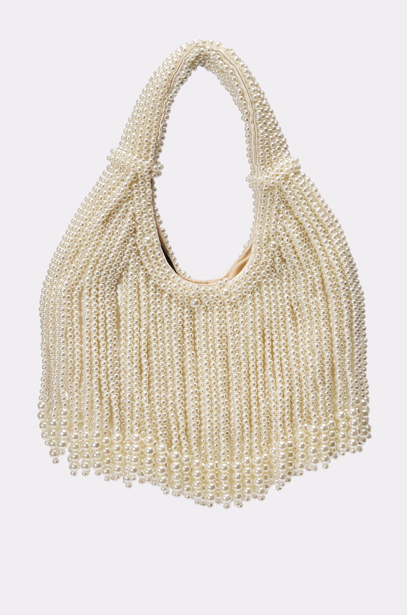 The ON A YACHT PEARL PURSE is a mini handbag adorned with ivory faux pearls, featuring a rounded handle and fringed texture, shown against a simple light background.