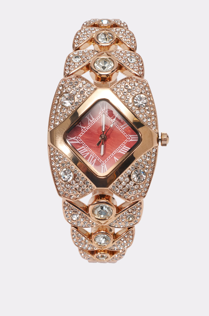 The ROSEY WATCH is a gold wristwatch with a red square face, Roman numeral markers, and a decorative band embellished with large clear gemstones and sparkling smaller stones.