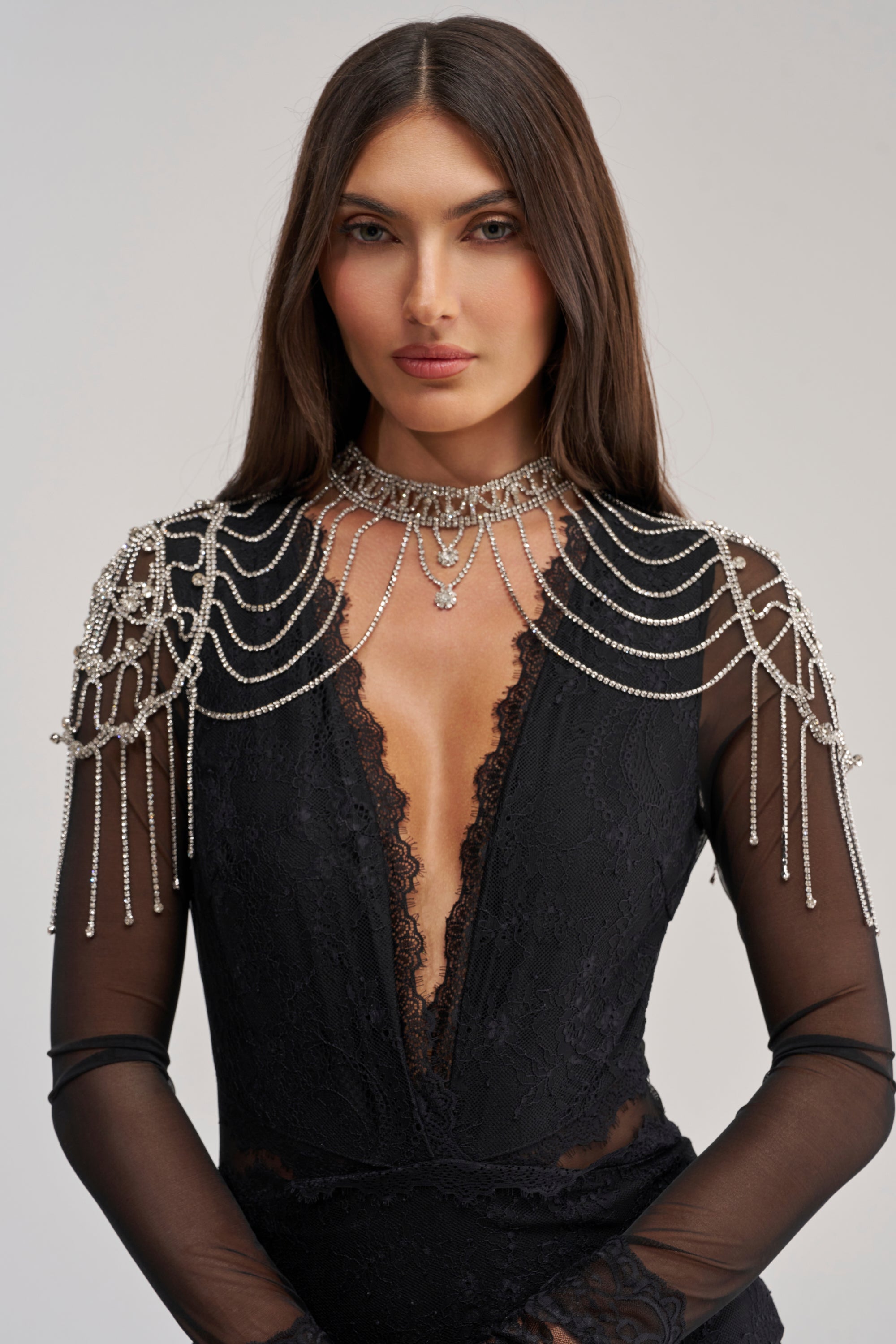 A woman with long brown hair wears the PAY MY BILLS BODY CHAIN, an ornate collar fringe body chain with draped strands and sparkling details over a sheer black lace dress—ideal statement festival jewelry.