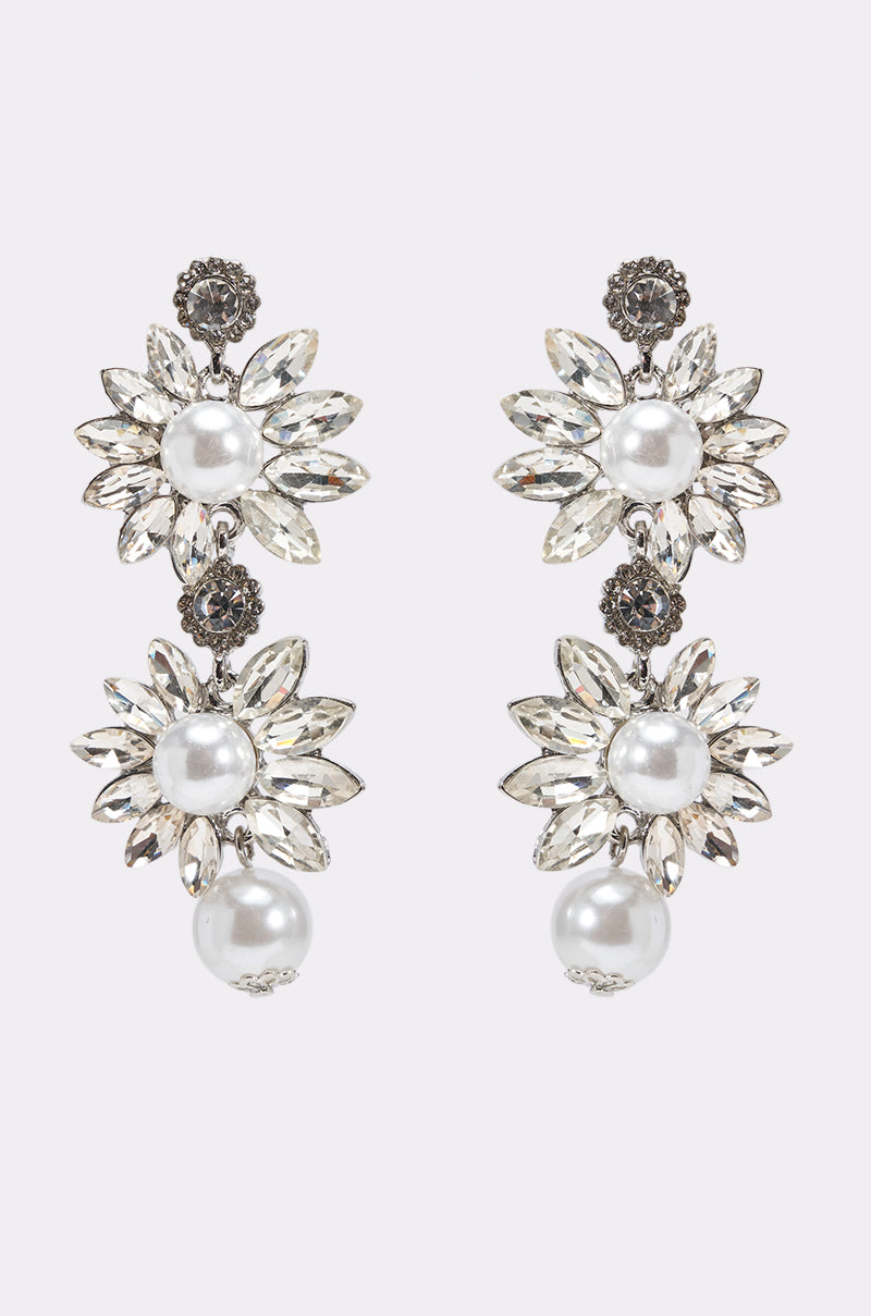 The TO THE GALA EARRING is a pair of ornate rhinestone drop earrings with floral designs, clear gemstone petals, large faux pearl centers, and a round pearl dangling from the bottom of each earring.