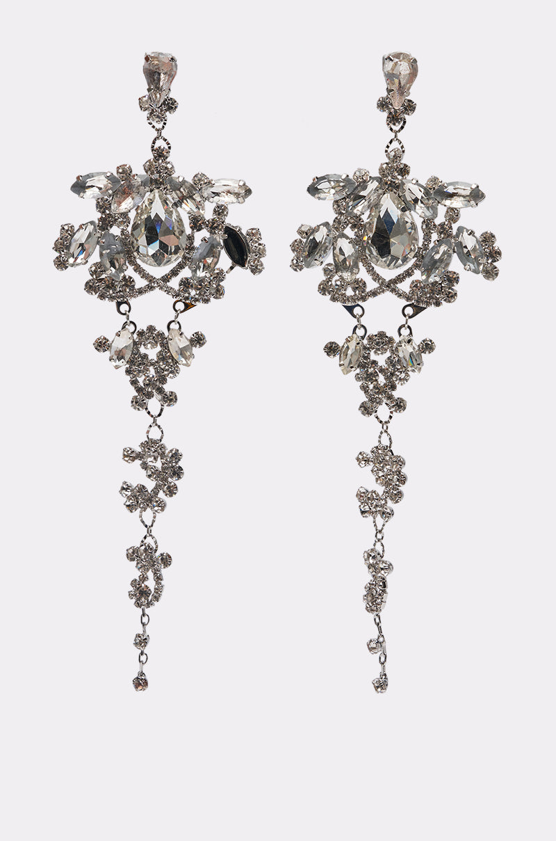 The LETS GO OUT EARRING is a pair of chandelier-style silver statement drop earrings with intricate floral patterns, long dangling elements, and multiple clear gemstones for added sparkle.