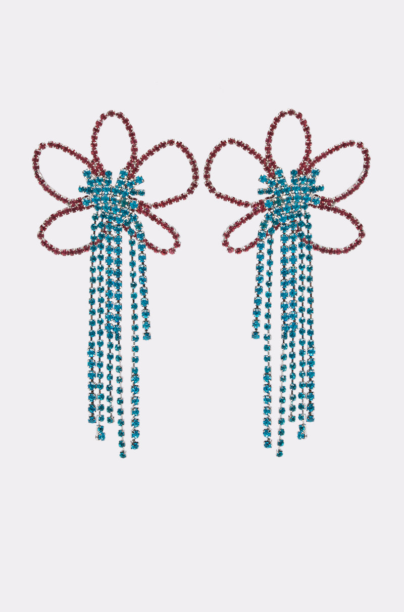 The FLOWER POWER EARRING features stylized bow shapes with red rhinestone loops and long blue tassels, adding playful sparkle to your summer look. Displayed on a white background.