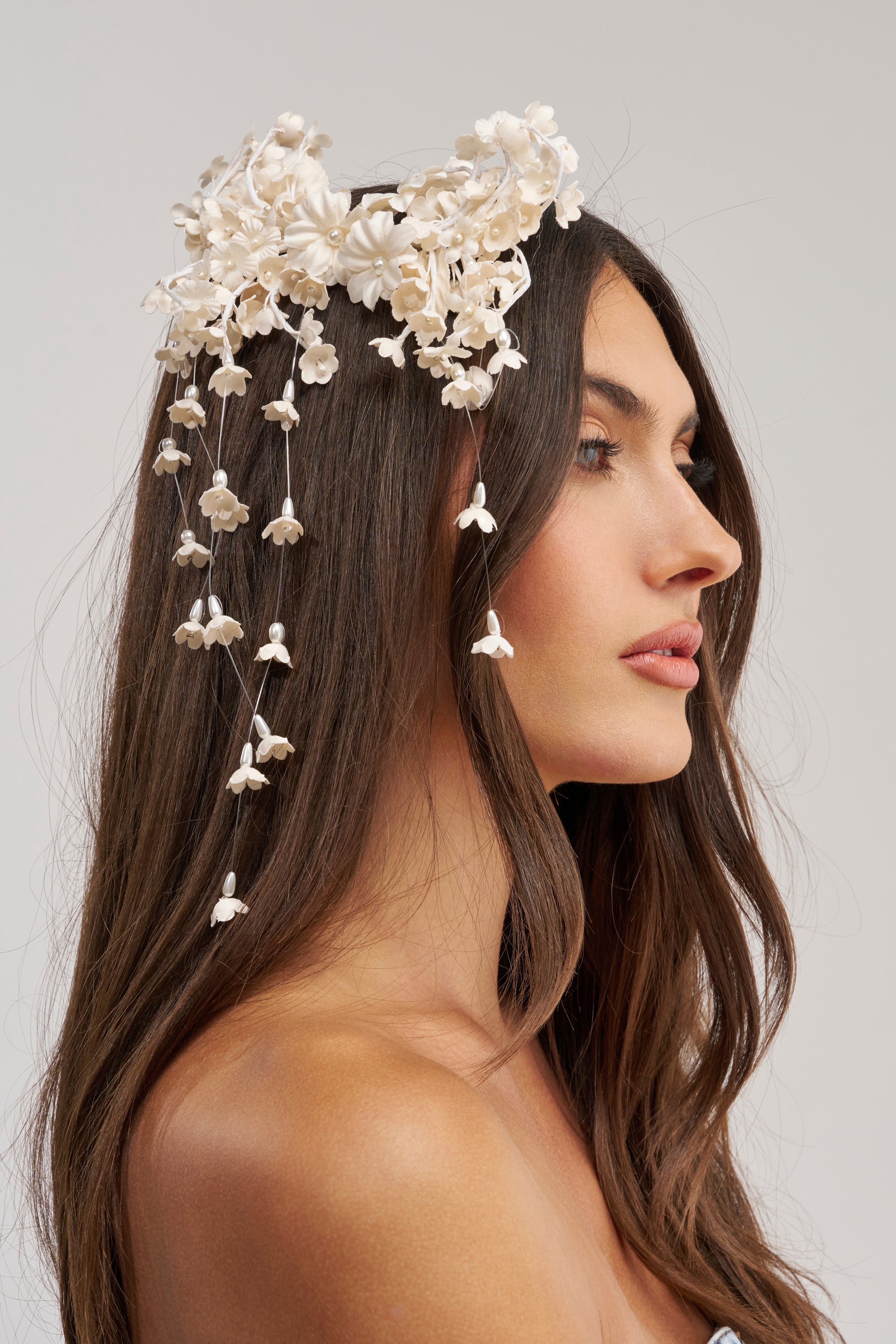 A woman with long brown hair wears the THRU THE GARDEN HAIR CLIP featuring white florals and a delicate butterfly, set against a light neutral background. She is shown in profile facing right.